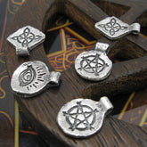 Handmade silver charms with inscribed pentagram, witch's knot, evil eye randomly arranged on dark wood background