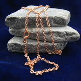 A copper cable chain with lobster clasp casually draped over flat grey rocks with a dark blue background.