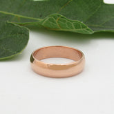 Front view of polished domed copper ring resting on a white surface with a blurry green leaf in the background.