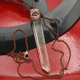Pendant of clear quartz point with inscribed copper cap and copper chain sitting on a black metal circle on shiny red background