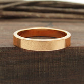 Front view of flat copper band ring sitting flat on dark wood block with twigs in background