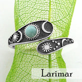 Front view of a wrap-around two-tiered oxidized silver ring with sun, moon, and stars design and bluish-green cabochon on lacy green leaf with white background