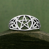 Front view of cut-out sterling silver Celtic style ring with pentagram resting on dark wooden rounded prop with dark green background.