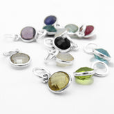 Close-up photo of random arrangement of multicolored faceted birthstone charms in silver settings against white background.