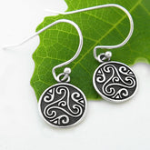 Silver earrings with intricate Celtic designs on a green leaf background