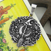 Front view of a round oxidized silver pendant with witch's broom and hat and crescent moon surrounded by flowers and stars resting on a yellow Tarot card with a wooden prop in the background
