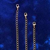Three copper chain extender links with lobster clasps, displayed vertically against a textured blue velvet background.