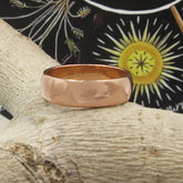 Front view of plain domed copper ring resting on a light-colored tree branch with a black and earth tone graphic in the background.