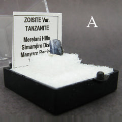 Angled view of specimen of blue tanzanite crystal labeled in plastic box on dark background