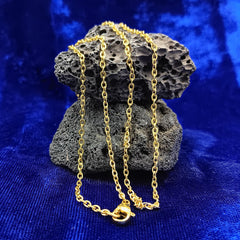 A gold chain necklace draped over a dark porous rock, set against a vibrant blue velvet fabric background.