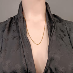 A delicate gold chain necklace displayed on a mannequin torso wearing a dark gray patterned silk robe against a neutral gray background.