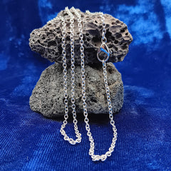 A stainless steel chain necklace draped over a dark porous rock, set against a rich blue velvet fabric background.