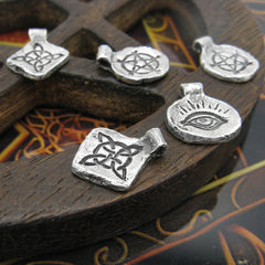 Handmade silver charms with inscribed pentagram, witch's knot, evil eye randomly arranged on dark wood background
