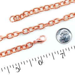A copper chain link bracelet or necklace shown on a white background with a US quarter coin and a ruler for scale.