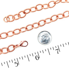 A copper chain link bracelet with a lobster clasp, shown on a white background with a coin and ruler for scale.