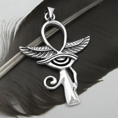Silver Egyptian Ankh with wings and Eye of Horus pendant on black feather with light background.