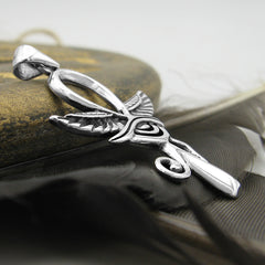 Side view of silver Egyptian Ankh with wings and Eye of Horus pendant leaning against golden stone on black feather with light background