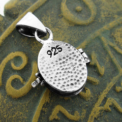 Rear view of a small silver locket with a hammered finish and inscribed with 925 resting on a rustic gold textured surface with raised symbols.