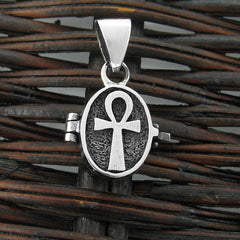 Front view of a small silver locket with a raised Ankh symbol resting on a dark woven basket.