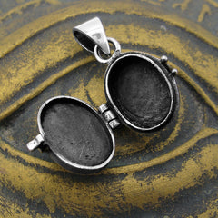 Inside view of an open small silver locket with a blackened interior finish resting on a rustic gold textured surface with raised eye shape.