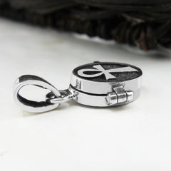 Side view of a small silver locket with a raised Ankh symbol resting on a white surface with a dark woven basket in background.