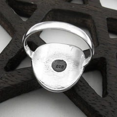 Back/inside view of polished sterling silver ring with black circle in center inscribed with 925 resting on a dark wooden lattice-like prop on a white background.