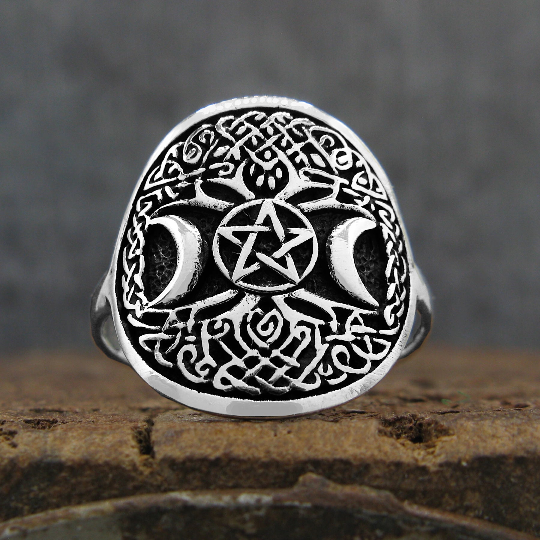 Front view of oxidized sterling silver ring with Celtic Tree of Life design and crescent moons and pentagram resting on rustic wood surface with dark grey background.