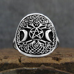 Front view of oxidized sterling silver ring with Celtic Tree of Life design and crescent moons and pentagram resting on rustic wood surface with dark grey background.