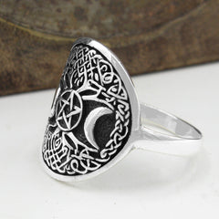 Side view of oxidized sterling silver ring with Celtic Tree of Life design and crescent moon resting on white surface with rustic wooden background.