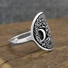 Side view of oxidized sterling silver ring with Celtic Tree of Life design and crescent moon resting on rustic wood surface with dark grey background.