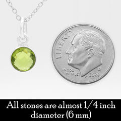 A silver necklace with a faceted light green gemstone pendant shown next to a U.S. dime to show scale