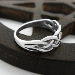 Angled side view of a silver ring with a braided Celtic knot design resting on dark wood lattice-like prop on a white background.
