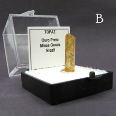 Side view of specimen of Brazilian 'honey' topaz gemstone labeled 'B' in plastic case on dark background.