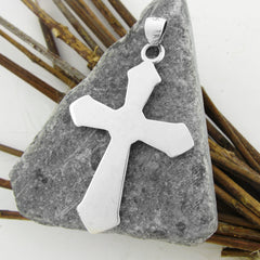 Opposite side of Silver cross pendant on a gray stone with wooden sticks in the background