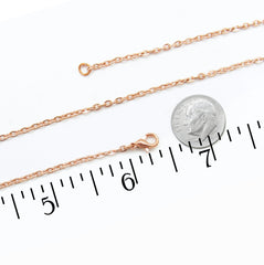 A copper chain necklace with a lobster clasp, shown alongside a US dime for scale and a black ruler measuring in inches on a white background.