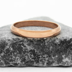 Domed copper band ring sitting flat on a  dark stone against a white background.