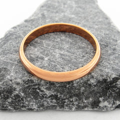 Overhead view of a domed copper band ring sitting flat on a dark triangular stone against a white background.