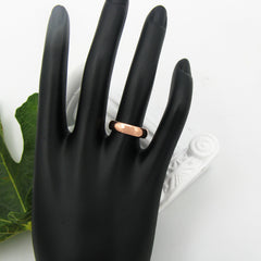 Polished domed copper band ring displayed on a black mannequin's hand with a green leaf and white column prop in background against a white backdrop.