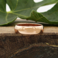 Front view of a polished domed copper ring resting on a dark block of rough wood with a blurry green leaf behind against a white background.