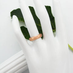 Polished domed copper band ring displayed on a white mannequin's hand with a green leaf and white column prop in background against a white backdrop.