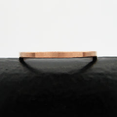 Slender flat faced copper band ring sitting flat on a black surface with a white background.