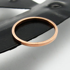 View from above of a slender flat faced copper band ring sitting flat on a black metal ring with a white background.