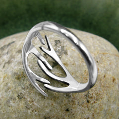View of the back and inside of a polished silver ring with a deer's antlers design resting on a round stone with a dark green background