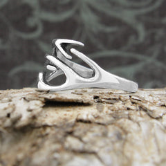 Side view of a polished silver ring with a deer's antlers design resting on a piece of rough tree bark with a black and green floral background