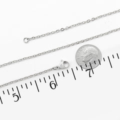 A silver chain necklace with a lobster clasp, shown alongside a US dime for scale and a black ruler with inch markings on a white background.