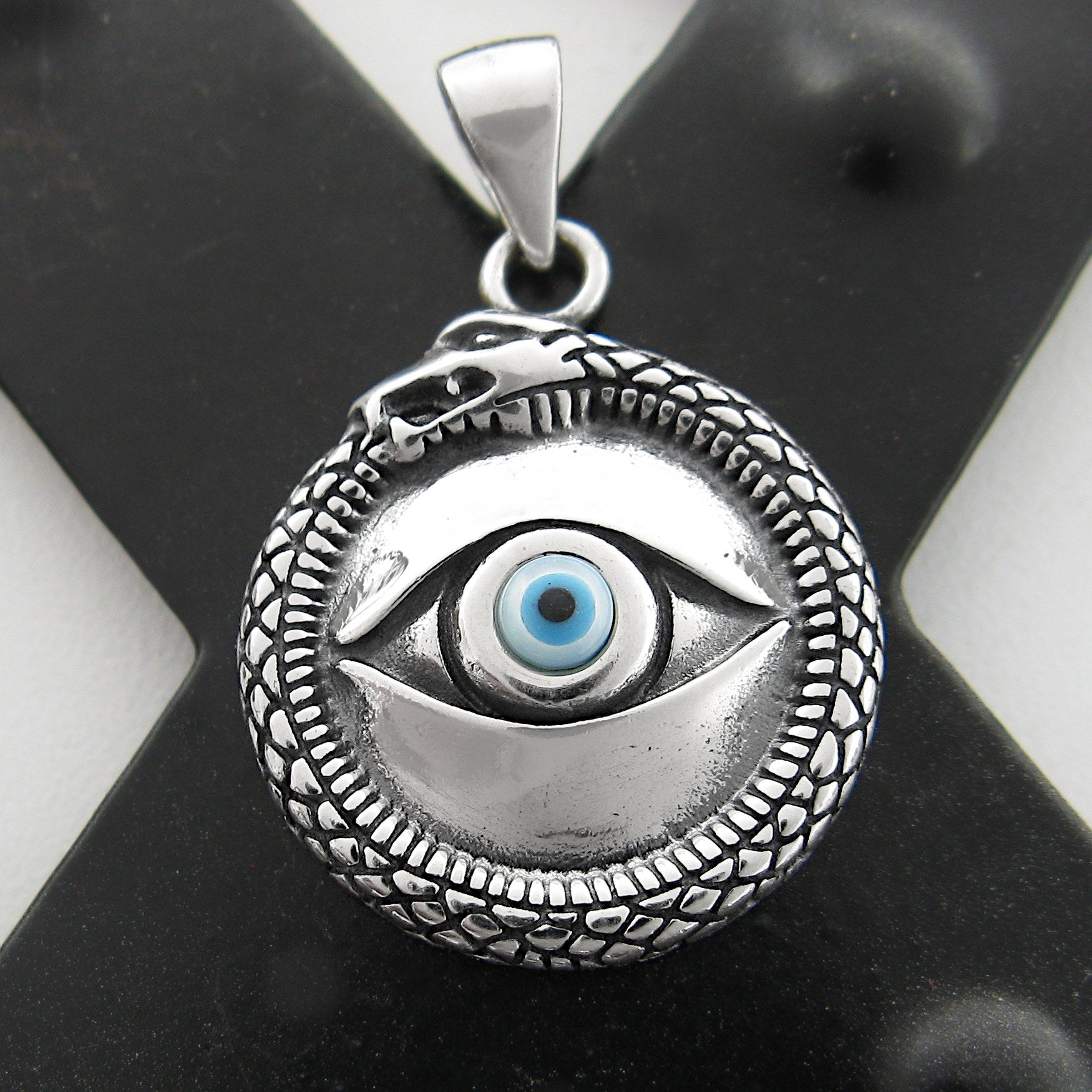 Front view of silver and blue evil eye pendant with snake border on a dark X background.
