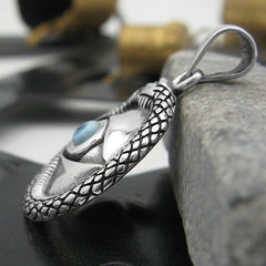 Side view of silver and blue evil eye pendant with snake border leaning on a stone on a mixed background.