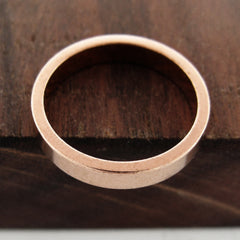 Overhead view of flat copper band ring sitting flat on dark wood block