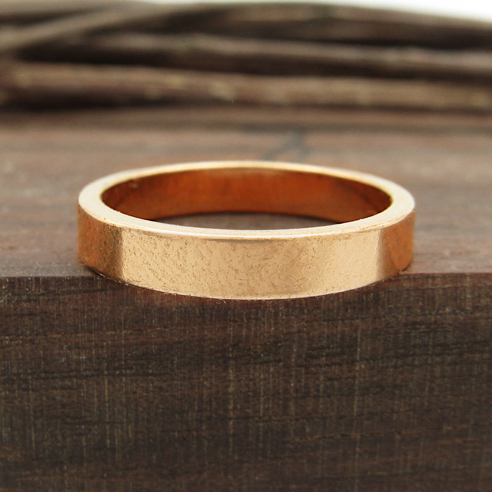 Front view of flat copper band ring sitting flat on dark wood block with twigs in background