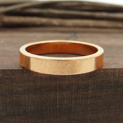 Front view of flat copper band ring sitting flat on dark wood block with twigs in background